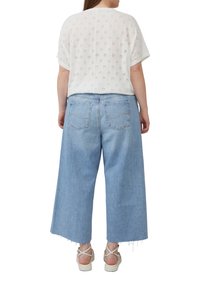 Witte top met korte mouwen, voorzien van een ajourpatroon en een ronde halslijn, gecombineerd met lichtblauwe flared jeans met rafelige zoom en achterzakken.