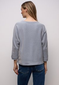 Gestreept lange mouwen top in lichtgrijs en blauw, met een brede halslijn en een ontspannen pasvorm met opgerolde manchetten. Draagt bij denim jeans.