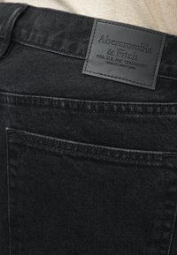 Schwarze Jeans aus Denim mit einem Lederlogo, das "Abercrombie & Fitch" trägt. Der Stoff hat eine glatte Textur und gestickte Details.