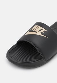Crne ljetne klapne s teksturiranim remenom s metalik zlatnim Nike logotipom, teksturiranim uloškom i izdržljivom gumenom potplatom.