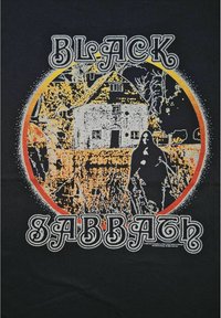 Zwarte T-shirt met een levendige, ronde grafiek van een huis, bomen en een figuur, in oranje, wit en zwart. Tekst luidt "BLACK SABBATH."