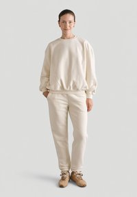 Kremowy sweatshirt i spodnie, wykonane z miękkiego materiału. Sweatshirt ma okrągły dekolt, opadające ramiona; spodnie są dopasowane i mają elastyczny pasek w talii.