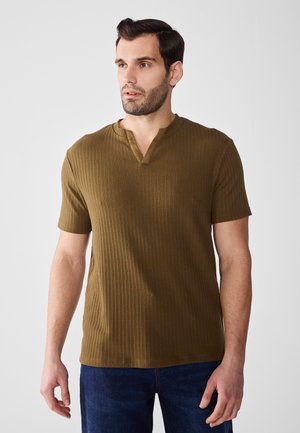 Tricou scurt din bumbac în verde măsliniu, cu guler notch. Țesătura pare moale și texturată. Asortat cu blugi albaștri.