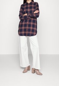 Navy plaid button-up shirt with orange and white accents. Paired with white wide-leg trousers and glossy beige block-heel shoes.