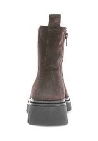 Brown suede ankle boot with a smooth texture, rounded toe, side zipper, and a thick black rubber sole. Features a pull tab on the back.