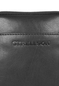 Borsa in pelle nera con superficie testurizzata, caratterizzata dal logo "Strellson" impresso. Chiusura con zip e dettaglio di cucitura a contrasto.