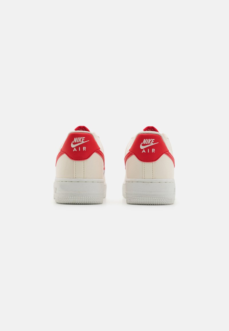 Weiße Nike Air Sneaker mit roten Akzenten, glattem Lederobermaterial, gepolstertem Absatz und strukturiertem Gummisohle. Schlichte Rückansicht.