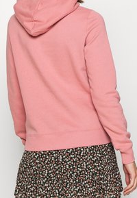 Rosa hoodie i mjukt tyg, med dragsko i huvan och ribbade ärmslut, kombinerad med en svart blommig kjol.