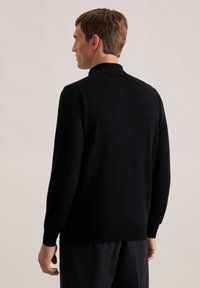 Schwarzer Strickpullover mit hohem Kragen und langen Ärmeln, von hinten präsentiert. Glatte Textur, taillierte Passform und gerippte Saumdetails.