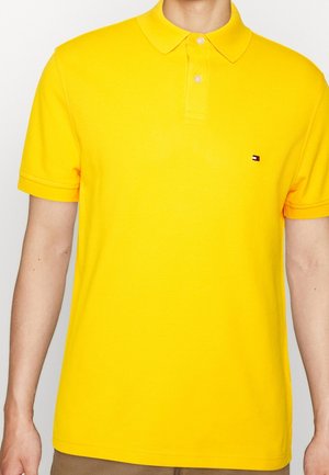 Polo shirt jaune en coton, avec un col classique, des manches courtes et un petit logo sur la poitrine gauche. Texture lisse.