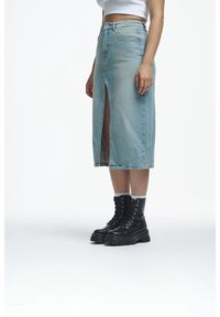 Denim midi skirt in light blue with a front slit. Paired with black chunky lace-up boots. Smooth texture and classic five-pocket design.