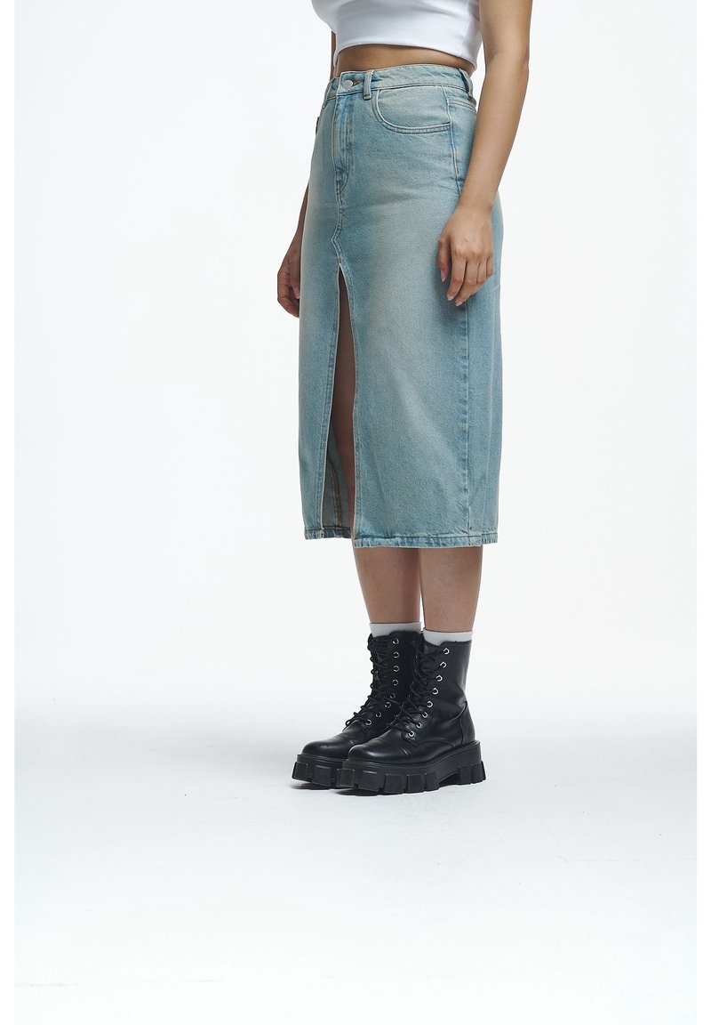 Denim midi skirt in light blue with a front slit. Paired with black chunky lace-up boots. Smooth texture and classic five-pocket design.