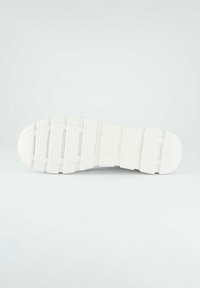 Bílá podrážka tenisky s texturovaným vzorem, obsahující drážky pro trakci a stabilitu. Hladký povrch s oble špičkou a patou.