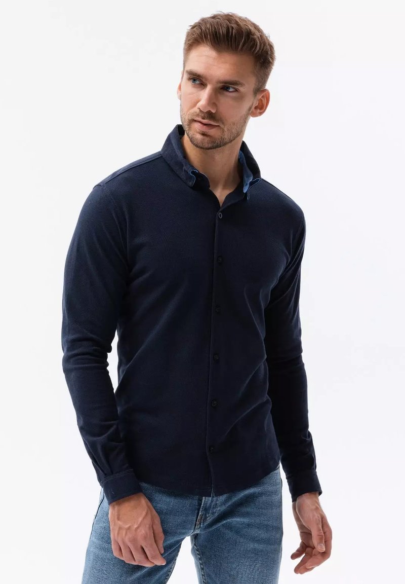 Maglietta a maniche lunghe blu navy con colletto, chiusura a bottoni e colletto interno blu a contrasto. Tessuto morbido con una trama testurizzata.