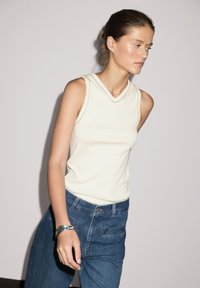 Cremefarvet ærmeløs top med V-halsdesign, parret med højtaljede blå denimjeans. Glat tekstur, minimale syninger.
