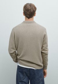 Beige gebreide trui met een geribde kraag en manchetten, met lange mouwen en een relaxed fit, gecombineerd met donkere spijkerbroek.