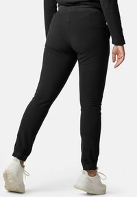 Schwarze, eng anliegende Sweatpants mit gerippten Knöchelbündchen und glatter Textur, kombiniert mit weißen Sportschuhen. Minimale Nähte sichtbar.