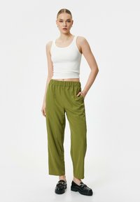 Witte geribbelde tanktop met spaghettibandjes en olijfgroene wijde broek met elastische tailleband en zijzakken. Zwarte chunky loafers.
