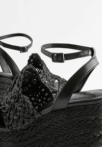 Schwarze geflochtene Keilsandalen mit einem strukturierten, gewebten Obermaterial, verstellbaren Fesselriemen und einer dicken, seilartigen Plattform.