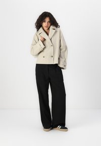 Beige cropped double-breasted jacket with large buttons, layered sleeves, paired with wide-leg black trousers and black shoes with white stripes.