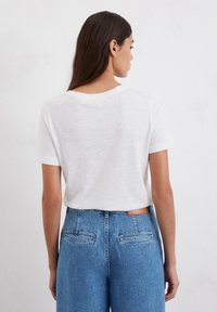 White short-sleeve t-shirt with a relaxed fit, made from lightweight material. Paired with high-waisted blue denim jeans with back pockets.