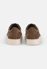 Zapatos de ante marrón de tipo slip-on con una suela de goma blanca de perfil bajo y bordes redondeados, que presentan una textura suave y un diseño minimalista.