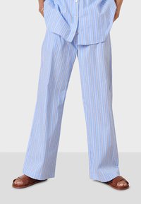 Ljusblå ränderade byxor med en lös passform, med tunna vertikala ränder i vitt och rött. Tillverkade av mjukt tyg, matchade med bruna sandaler.