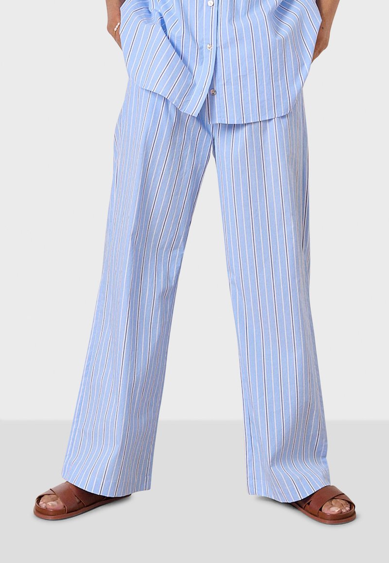 Ljusblå ränderade byxor med en lös passform, med tunna vertikala ränder i vitt och rött. Tillverkade av mjukt tyg, matchade med bruna sandaler.