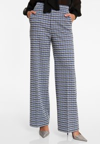 Pantalons à carreaux bleus et blancs à jambe large avec poches avant, taille haute et tissu lisse, associés à des chaussures argentées à bouts pointus.