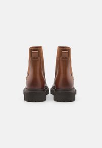 Bottines en cuir marron avec panneaux élastiques sur les côtés, semelle en caoutchouc noir texturé, et languettes à l'arrière pour un enfilage facile.
