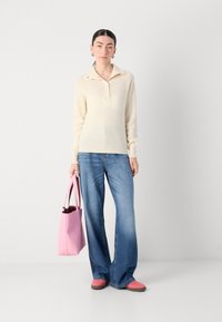 Un pull à col crème en tricot, un jean évasé bleu et un sac fourre-tout rose. Les chaussures sont des mocassins roses avec des semelles marron. Design simple, peu de détails.