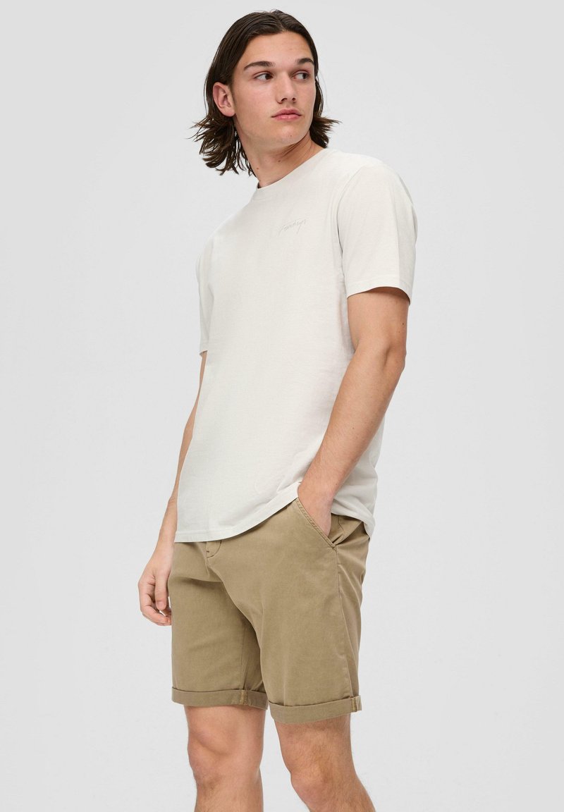 Helles graues Baumwoll-T-Shirt mit kurzen Ärmeln, Rundhalsausschnitt und dezentem Logo. Kombiniert mit khakifarbenen Baumwollshorts mit aufgerollten Säumen.