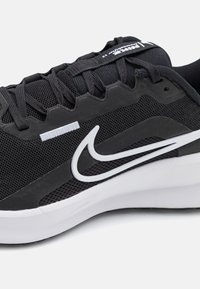 Schwarzer Sportschuh mit Mesh-Obermaterial, Gummielementen und einem weißen Nike-Logo. Verfügt über strukturierte Schnürsenkel und eine robuste weiße Sohle.