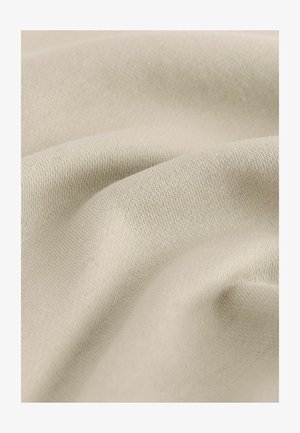 Közeli kép egy bézs, puha szövetekről, finom kötött textúrával és lágy redőkkel.