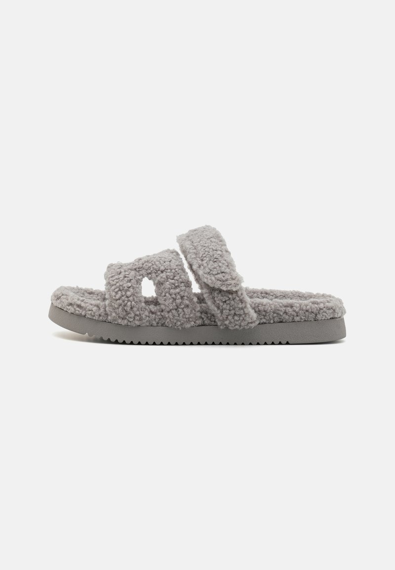 Chinelas cinzentas felpudas com duas tiras largas com secções recortadas. Material texturizado e sola de borracha com borda serrilhada.