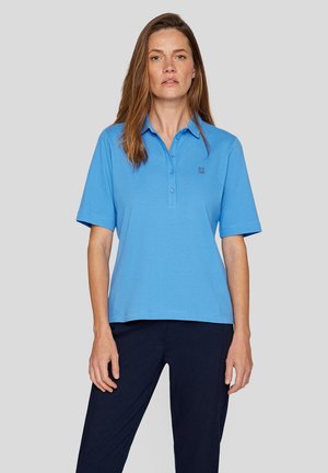 Hellblaues Kurzarm-Polohemd mit Knopfleiste und gesticktem Logo auf der Brust. Glattes Material, lässige Passform, kombiniert mit dunklen Hosen.