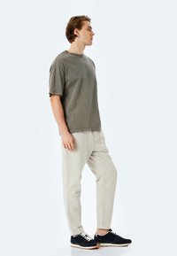 Camiseta verde oliva de manga corta, pantalones beige claros y zapatillas azul marino. Ajuste casual con una textura suave y un diseño simple.