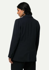 Blazer marine avec un design structuré, col cranté, manches longues et poignets boutonnés. Présente une couture arrière droite et une texture de tissu lisse.