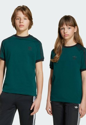 Zwei Kinder tragen kurzärmelige, dunkelblaugrüne T-Shirts mit schwarzen Akzenten und einem kleinen Logo. Der Stoff sieht glatt und leicht elastisch aus.