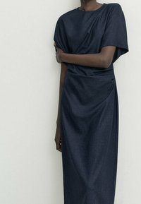 Dunkelblaues, knielanges Kleid aus weichem, strukturiertem Stoff. Mit einem Bootsausschnitt und lässigen, drapierten Ärmeln. Hoch tailliertes Design.