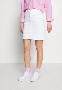 Jupe en denim blanc à coupe droite, avec fermeture à boutons sur le devant et détails de couture subtils. Associée à des baskets blanches et des chaussettes roses.