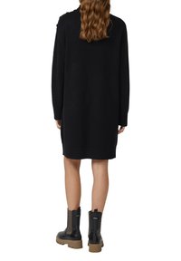 Zwarte gebreide sweater jurk met een losse pasvorm, lange mouwen en geribde manchetten en zoom. Gecombineerd met zwarte enkellaarsjes met een dikke zool.