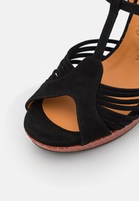 Sandale ouverte en daim noir avec plusieurs fines lanières, semelle intérieure rembourrée beige et semelle extérieure marron texturée, vue en gros plan.