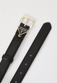 Black leather belt featuring a gold buckle with a triangular design and "GUESS" logo. Smooth strap with several adjustment holes.