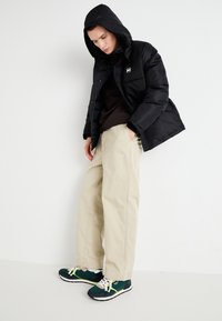 Black puffer jacket with a hood, tan wide-leg trousers, and green sneakers with beige accents. The jacket features a small logo on the chest.