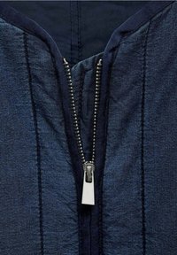 Vêtement bleu marine à fermeture éclair métallique. Présente des lignes de couture verticales et un tissu texturé, offrant un aspect structuré.