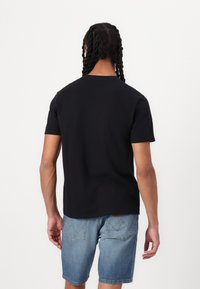 Camiseta preta de manga curta com decote redondo, combinada com calções de ganga. O tecido parece sólido e suave com um corte simples.