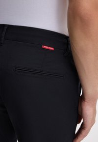 Czarne dżinsy z tylnią kieszenią i czerwoną metką "JOOP! JEANS". Tkanina ma gładką fakturę i dopasowany krój.