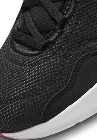 Detailní záběr na přední stranu černé síťové tenisky s texturovanou tkaninou, černými šněrovadly a bílým okrajem podrážky s malým růžovým detailem na špičce.