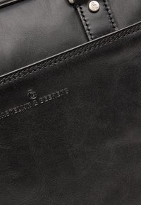 Zwarte leren handtas met een soepele textuur, subtiele stiksels en een reliëf logo-detail. Inclusief metallic hardware accenten.